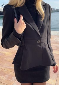 Blazer preto ajustado com design justo, fecho de botão único e cintura peplum, combinado com uma saia mini preta canelada.