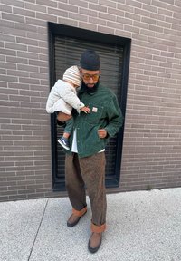 Πράσινο καπιτονέ μπουφάν με τσέπη, καφέ παντελόνι με λεοπάρ εκτύπωση και καφέ παπούτσια. Ένα παιδί σε ανοιχτό καπιτονέ μπουφάν κρατιέται.