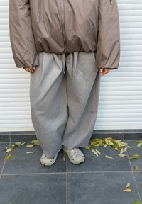 Brun puffed jakke med lynlås, kombineret med løstsiddende grå joggingbukser. Outfittet kompletteres af cremefarvede sneakers og spredte blade nedenunder.