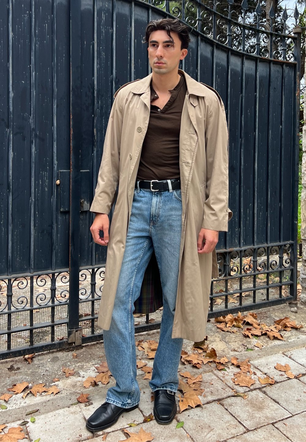 Beige trench coat barna ing felett, kék farmerrel párosítva. Fekete öv és cipő egészíti ki a megjelenést. A kabát belső bélése kockás.