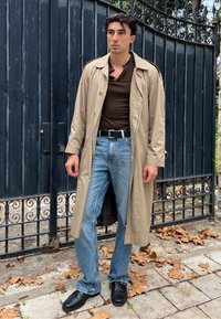 Beige trench coat barna ing felett, kék farmerrel párosítva. Fekete öv és cipő egészíti ki a megjelenést. A kabát belső bélése kockás.