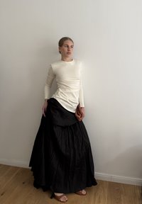 Kremna majica z dolgimi rokavi in nabrano oblačnostjo, združena z ohlapno črno maxi krilo, ki ima teksturirano tkanino in nabirano zasnovo.