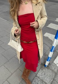 Piros pánt nélküli ruha, réteges szegéllyel, bézs velúrból készült kabát, barna térd fölé érő csizma, kis fehér kézitáska, arany láncos öv, réteges nyakláncok.