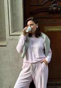 Vaaleanpunainen vapaa-ajan vaatesetti, joka on valmistettu pehmeästä kankaasta. Settiin kuuluu pitkähihaiset paita ja joustavyötäröiset housut. Harmaa huivi on heitetty hartioille.