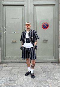 Μπλουζάκι με κοντό μανίκι σε ριγέ σχέδιο και αντίστοιχες σορτσάκι σε σκούρους τόνους, συνδυασμένα με ένα λευκό μπλουζάκι, αξεσουάρ, γυαλιά ηλίου και μαύρα παπούτσια.