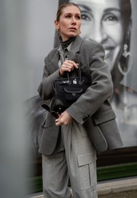 Grå överdimensionerad kavaj över en ljusgrå skjorta, i kombination med lösa gråbyxor. Håller en svart handväska med silverdetaljer och solglasögon med sköldpaddsram.