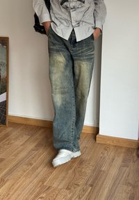 Jeans in denim blu chiaro dal taglio relax e leggermente sbiaditi, con delicate sfumature, abbinati a sneakers bianche chunky e una borsa a spalla nera.