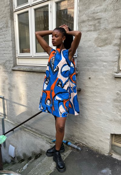Un vestido sin mangas con un audaz patrón abstracto que presenta colores azul, naranja y negro, hecho de una tela con una textura ligera.