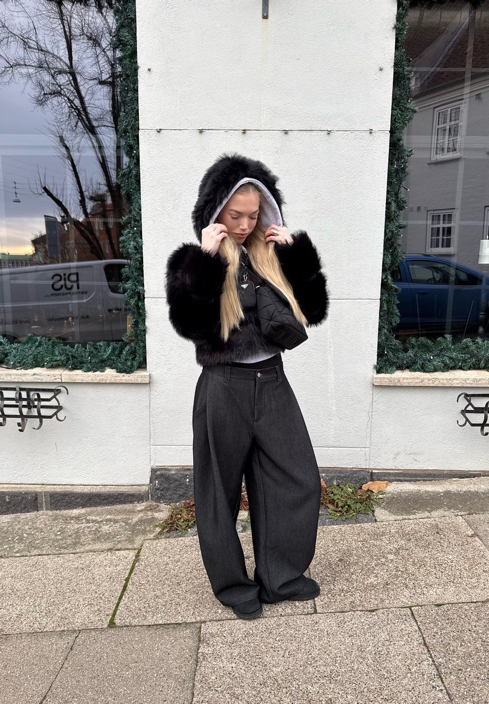 Jachetă cu glugă din blană artificială neagră cu căptușeală gri, asortată cu pantaloni supradimensionați gri închis și o poșetă neagră mică de purtat încrucișat.
