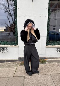 Jachetă cu glugă din blană artificială neagră cu căptușeală gri, asortată cu pantaloni supradimensionați gri închis și o poșetă neagră mică de purtat încrucișat.