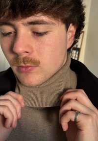 Lys brun ribstrikket rullekravesweater med en tætsiddende pasform. Hænder holder i kraven og fremviser en sølvring på den ene hånd. Blød tekstur.