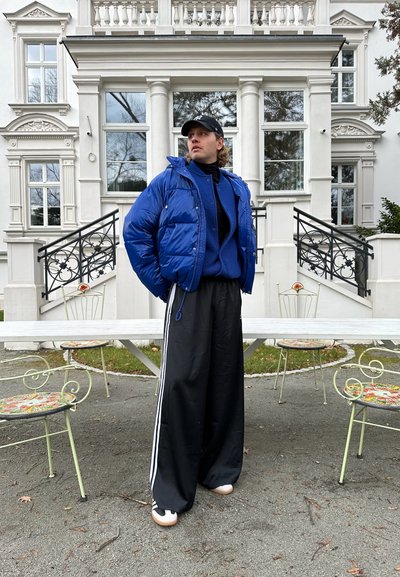 Chaqueta acolchada azul con capucha, combinada con un suéter texturizado azul, pantalones de pierna ancha negros y zapatillas blancas con detalles negros.