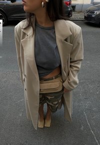 Beige oversized jas, grijs cropped top, camouflage shorts en naakte blokhak schoenen. Bevat een tan heuptas en grote oorbellen.