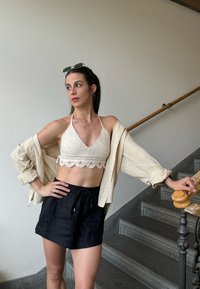 Crochet halter top in cream with scalloped edges, teamed with black linen shorts and a beige open shirt, set against a staircase backdrop.