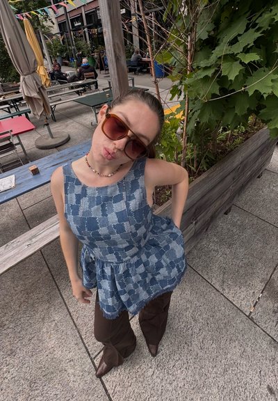 Vestido azul claro con estampado y falda acampanada, combinado con pantalones acampanados marrones y zapatos de punta marrones. Grandes gafas de sol marrones completan el look.