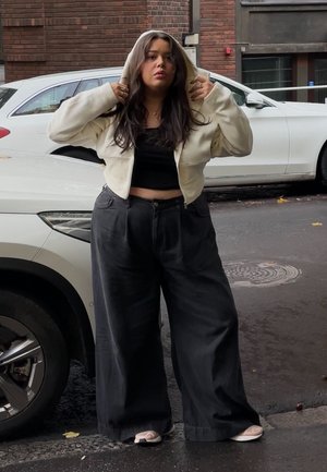 Sudadera corta color crema con cordón y una camiseta negra, combinadas con pantalones negros sueltos y zapatos tipo slip-on de color claro.