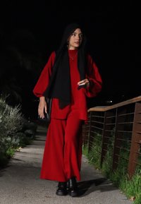 Vörös, bő fazonú felső és széles szárú nadrág fekete hijabbal és vastag fekete csizmával párosítva. Sétálás egy úton éjszaka.