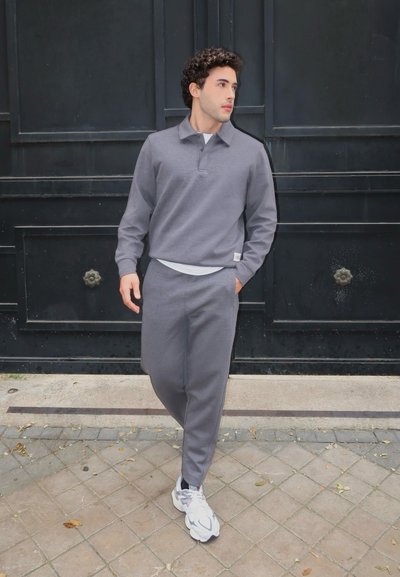 Conjunto de sudadera y pantalones de chándal grises, con cuello y puños acanalados, combinado con zapatillas blancas; tejido texturizado con un ajuste relajado.