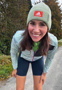 Αθλητική εμφάνιση που περιλαμβάνει ένα ανοιχτό πράσινο πλεκτό σκουφάκι, μία μοτίβο ζακέτα σε αποχρώσεις του πράσινου και εφαρμοστά ναυτικά σορτς με πλαϊνές μανσέτες.