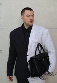 Svart og hvit blazer med design, svart skjorte og en svart håndveske med frynser. Glatte og teksturerte stoffelementer synlige.