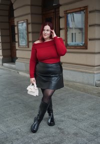 Κόκκινο εκτός ώμου ριμπ πουλόβερ, μαύρη δερμάτινη μίνι φούστα, μαύρες γόβες μέχρι το γόνατο, κρατώντας μια λευκή τσάντα με αλυσίδα.