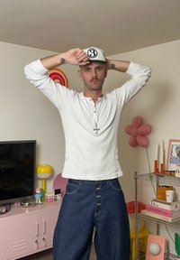 Cămașă Henley cu mâneci lungi, de culoare albă, textură u�șoară, asortată cu blugi evazați de culoare albastru închis, cu nasturi în față. Accesorii: șapcă albă cu un logo negru.