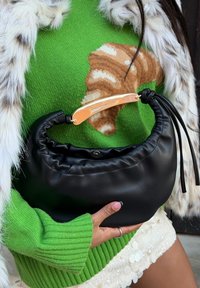 Sac à main en cuir noir avec un design plissé, une poignée ornée d'accents dorés et une fermeture. Le sac présente une texture douce et une silhouette élégante.