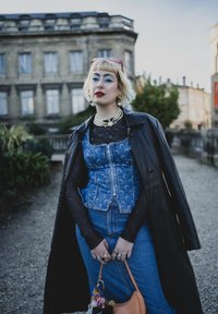 Blå jeanskorsett med mån-mönster, svarta nät-långa ärmar, lång svart läderrock, jeansbyxor och en orange handväska med accessoarer.