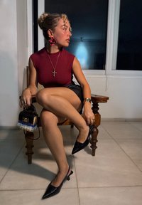 Bordeaux höghalsetopp, svarta lädershorts, svarta slingbackklackar, stora röda blommörhängen, korshalsband och liten mönstrad handväska.