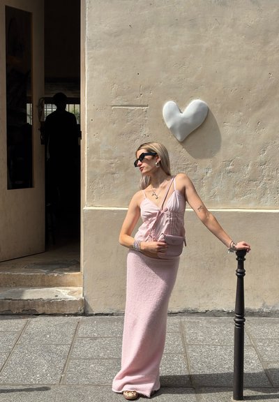 Falda maxi de punto rosa y top a juego con tirantes finos, superficie texturizada, combinado con un pequeño bolso rosa frente a una pared texturizada con un corazón blanco.