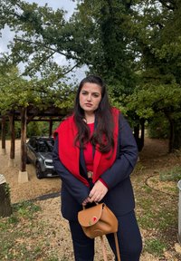 Blazer blu scuro sopra un top rosso, abbinato a jeans scuri e una borsa marrone. L'outfit presenta un scialle rossa lavorato a maglia con una texture a coste.