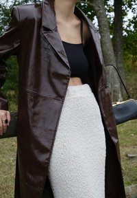 Marron long coat in faux leather, black crop top, and a white textured knit skirt; accessories consist of a small black handbag with gold hardware.