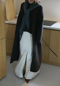 Dolgi temen plašč preko temnega puloverja, v kombinaciji z belo krilo s sprednjim razporkom. Obleko dopolnjuje sivi šal, obutev pa so rjave čevlje z detajli.