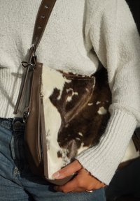 Pruun nahast ja lehmanahast õlakott, millel on lukuga tasku ja tekstuurse mustriga pind. Reguleeritav rihm metallist tarvikutega.