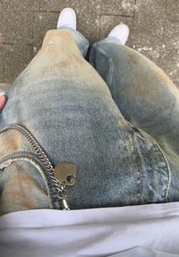 Φθαρμένο μπλε τζιν παντελόνι με άνετη γραμμή, που διαθέτει ασημένιο κλειδοχέρι και μια μικρή τρύπα στον δεξί μηρό, συνδυασμένο με ένα λευκό πουκάμισο.