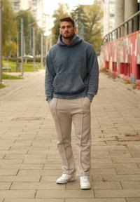 Mikina s kapucí ve vybledlé modré barvě, doplněná o světlé béžové, šité joggingové kalhoty. Bílé tenisky dotvářejí celý outfit. Texturovaná tkanina, volný střih.