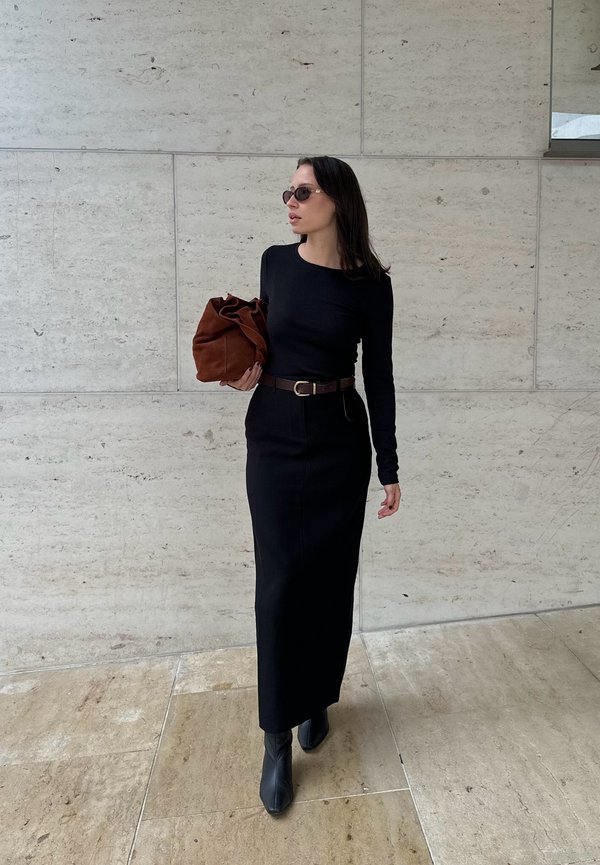 Vestido preto de manga longa com corpete ajustado e corte reto, combinado com uma mala de camurça castanha e botas de tornozelo pretas com bico fino.