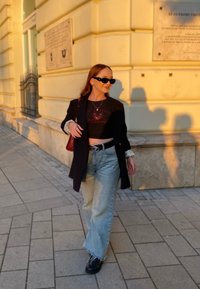 Μαύρο σακάκι πάνω από ένα μαύρο γραφικό κοντό μπλουζάκι, μπλε φαρδιά τζιν παντελόνια και μαύρες μπότες. Τα αξεσουάρ περιλαμβάνουν γυαλιά ηλίου και μια κόκκινη τσάντα.