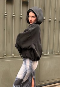 Schwarzer übergroßer Hoodie mit Kordelzug, getragen über einem gemusterten grau-weißen Rock mit Seitenschlitz. Glatter Stoff, lässige Passform.