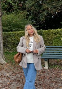 Ruudullinen bleiseri ruskean ja valkoisen sävyissä valkoisen collegepaidn päällä, yhdistettynä sinisiin levenevä lahkeisiin farkkuihin. Kädessä ruskea käsilaukku ja aurinkolasit.