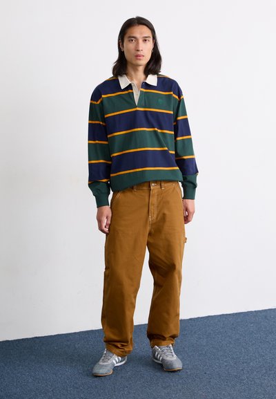 Polo de manga larga a rayas en azul marino y verde con cuello crema, combinado con pantalones cargo anchos en marrón y zapatillas deportivas grises.