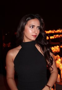 Haut noir à col halter, tissu lisse, coupe ajustée, cheveux longs et ondulés foncés, maquillage discret, fond à la lumière chaude des bougies.