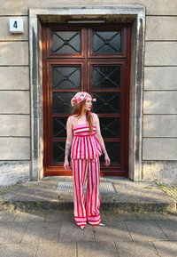 Sarkans un balts svītrots pepluma tops ar atbilstošām platajām biksēm; viegls audums; rakstains galvas lakats ar ziedu dizainu; ielu vide.