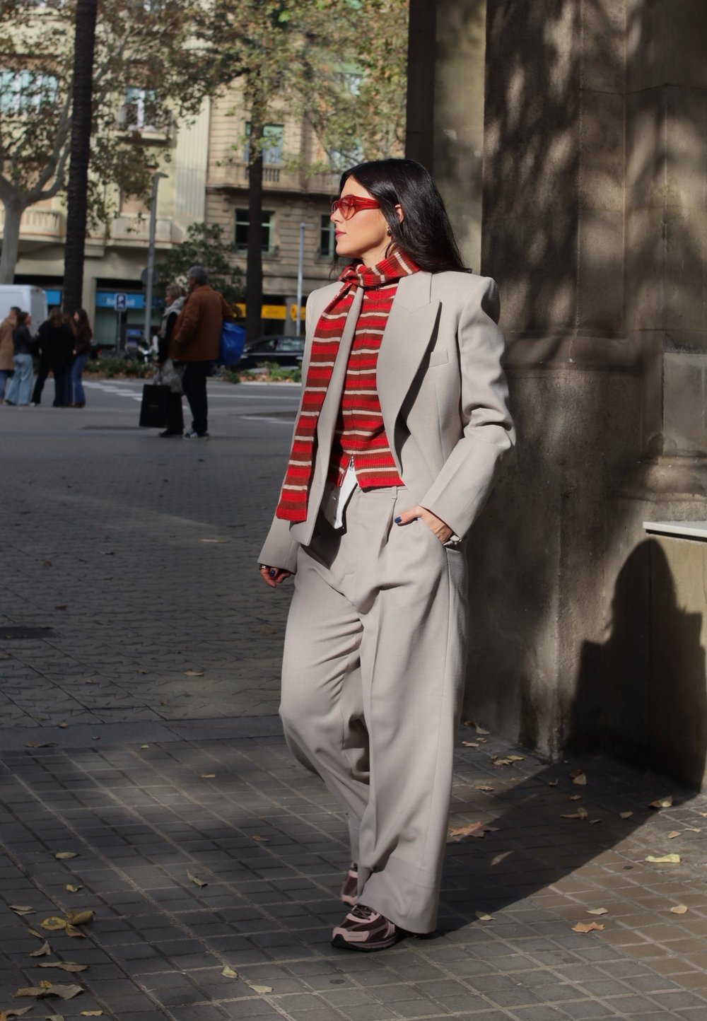Lichtgrijs op maat gemaakt pak met wijde broekspijpen, gecombineerd met een rood en beige gestreepte sjaal. Felrode bril en casual schoeisel.