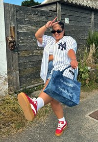 Denim tote bag featuring a "SAMSØE" print, paired with a white striped jersey, blue shorts, and red sneakers with white accents and gum soles.