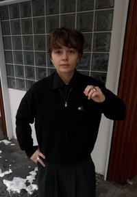 Cardigan noir zippé avec une finition texturée, doté d'une petite écusson logo. À associer à une chemise noire et un pantalon taille haute.