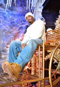 Un mannequin est assis sur une chaise en métal doré, portant un pull blanc en maille torsadée et un jean bleu clair déchiré, avec des bottes marron clair et un bonnet blanc.