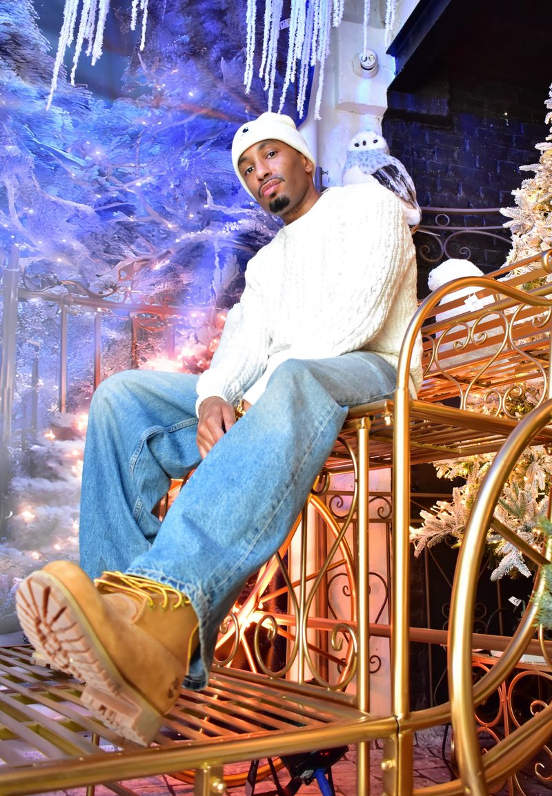 Un mannequin est assis sur une chaise en métal doré, portant un pull blanc à torsades, un jean bleu clair usé, des bottines marron clair et un bonnet blanc.