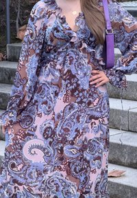 Abito lungo e fluido con un motivo paisley in tonalità di blu, viola e marrone. Progettato con volant e maniche lunghe.