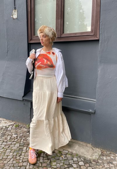 Camisa blanca de mangas largas sobre una camiseta de tirantes con un gráfico de labios rojos, combinada con una falda fluida de color crema y zapatillas rosas.
